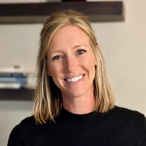 Portrait of a smiling blonde woman with shoulder-length hair, wearing a black top.